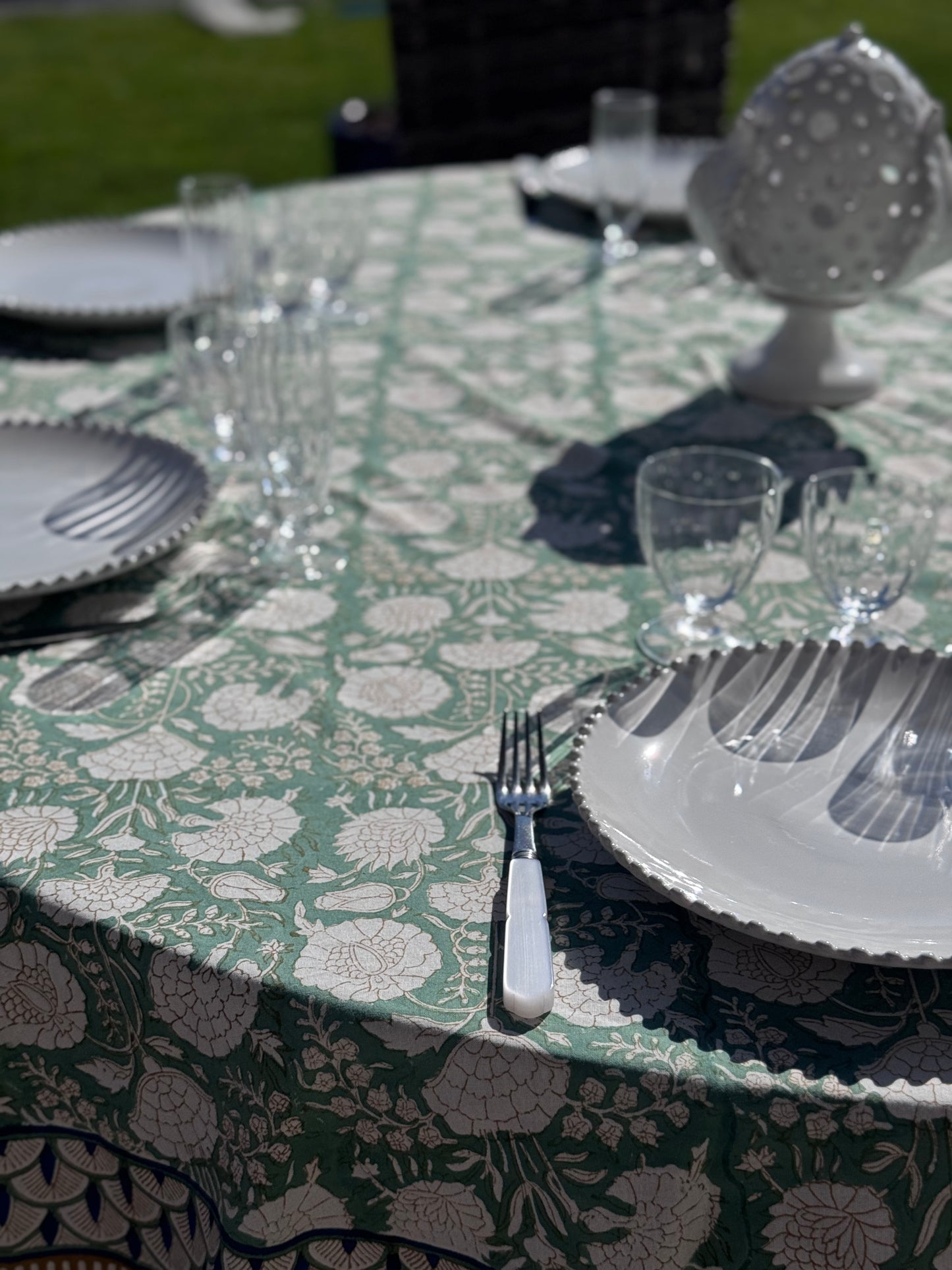 Gros plan sur la nappe Jaipur dressée sur une table ronde en extérieur avec de la jolie vaisselle blanche 