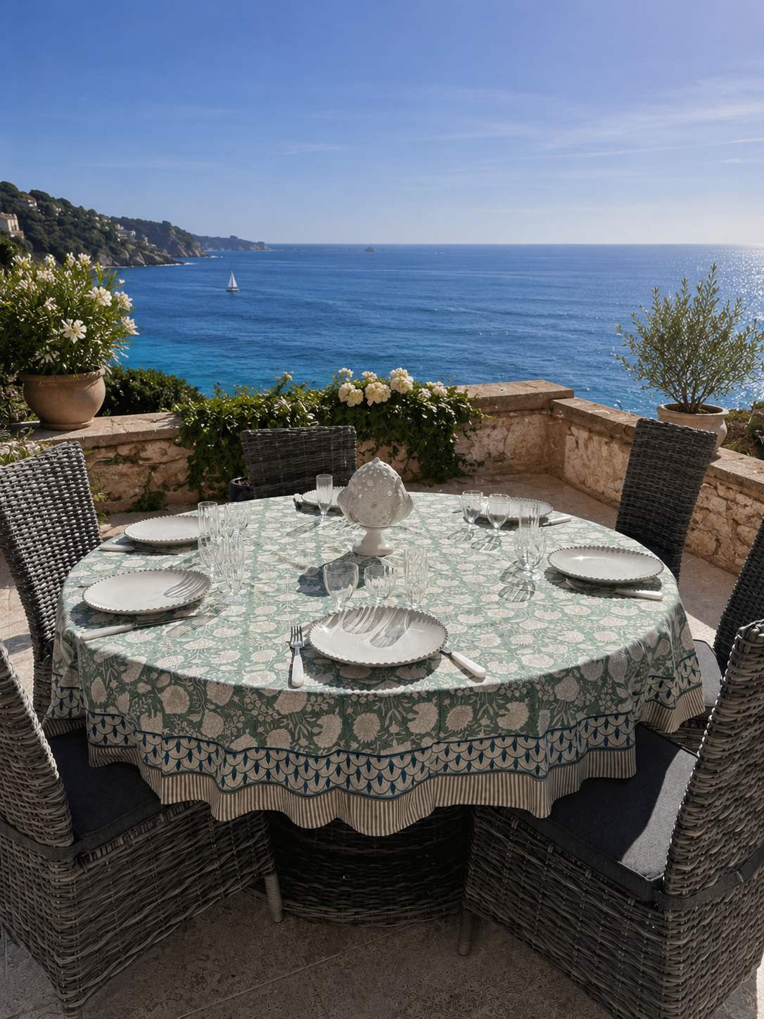 La nappe Jaipur vert sauge en coton block print  est présentée sur une grande table ronde sur une terrasse avec vue sur la méditerranée