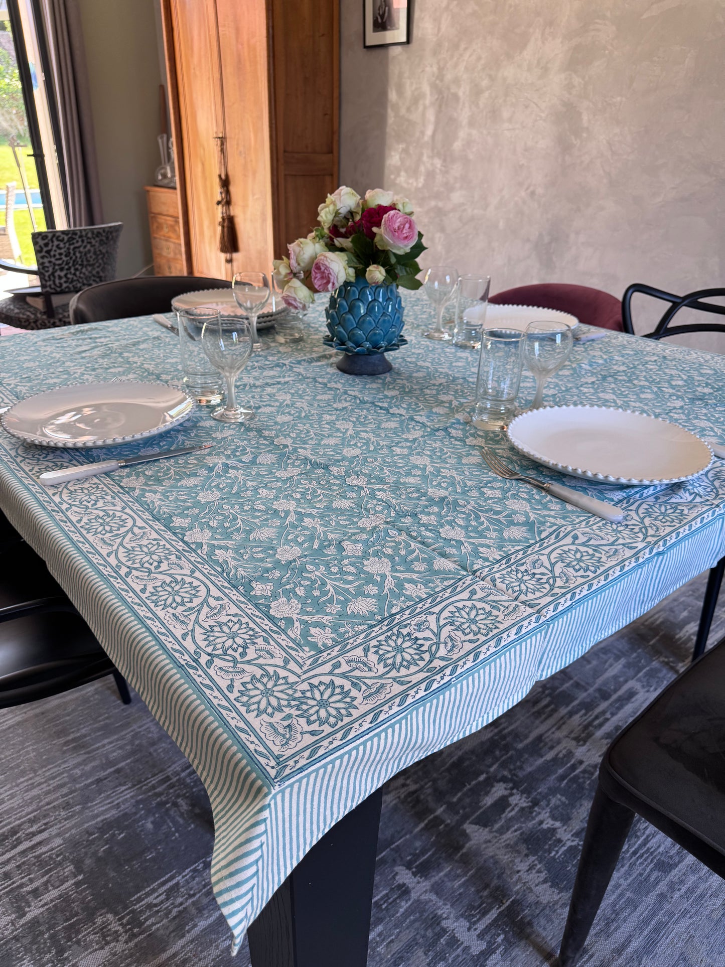 Présentation de la nappe Padma bleu en coton imprimé artisanalement sur une table carrée dans une salle a manger moderne.