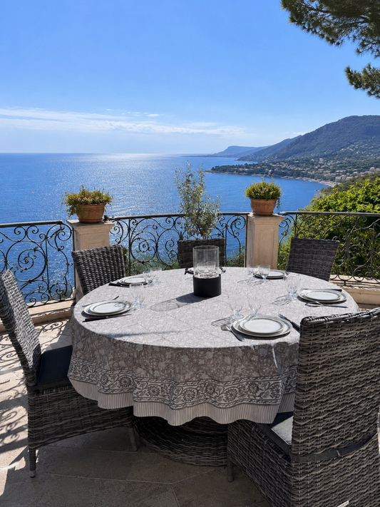 Nappe ronde Dehli beige en coton imprimée au blockprint présentée sur une table ronde sur une  terrasse avec vue sur la méditerranée 