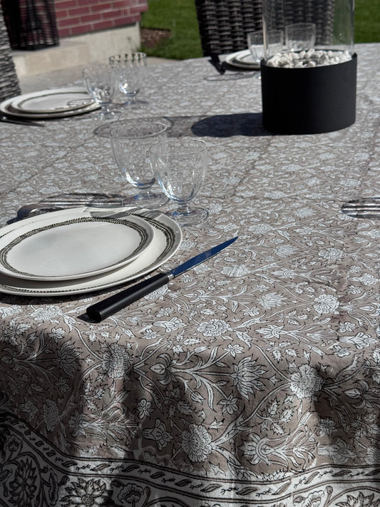 Nappe Dehli en coton beige sur une jolie table ronde dressée avec de la vaisselle et verres en cristal