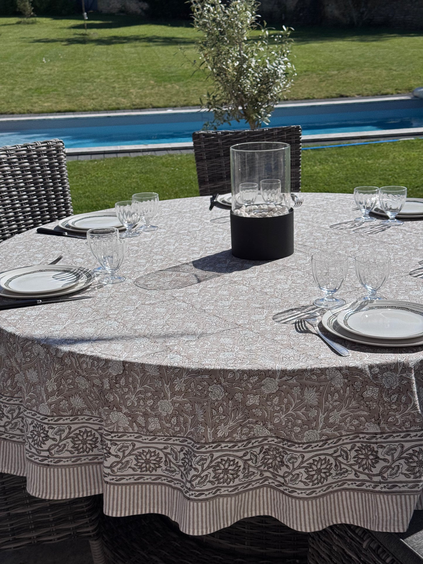 Nappe Dehli en coton beige sur une table ronde dans un jardin avec en arrière plan une piscine