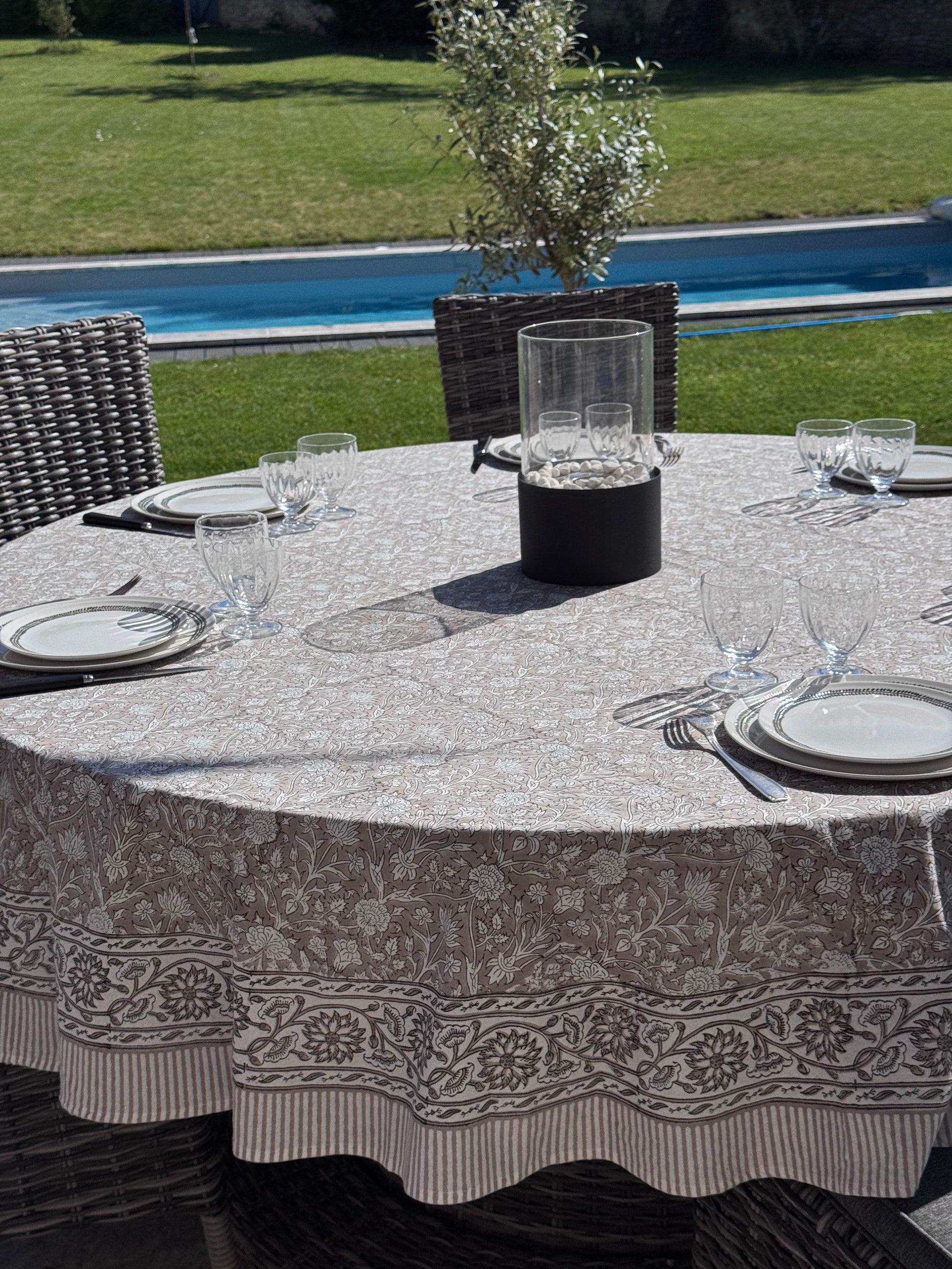 Nappe Dehli en coton beige sur une table ronde dans un jardin avec en arrière plan une piscine