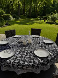 la nappe imprimée en Inde, modèle LOUS en block-print noir et blanc, disposée sur une table ronde dans un jardin verdoyanrt proche d'un sous bois