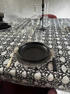 présentation de la nappe lotus sur une table carrée dans une salle à manger moderne avec de la vaisselle assortie couleur noire et blanche et pour décoration 2 carafes en cristal et un chandelier pour un résultat épuré, sobre et moderne 