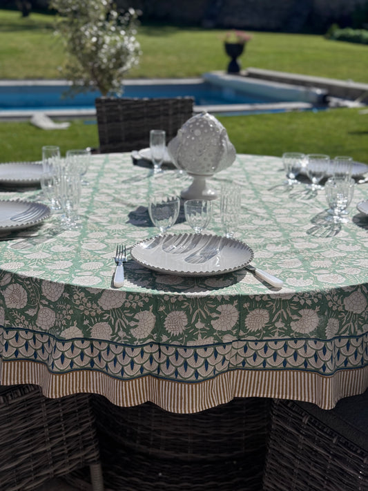 Mise en scène de la nappe verte Jaipur en coton block print avec de la vaisselle blanche et  un jardin avec piscine en arrière plan.