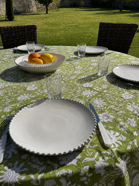 Nappe  Khushi verte présentée sur une table ronde en extérieur avec de la vaisselle blanche et quelques fruits